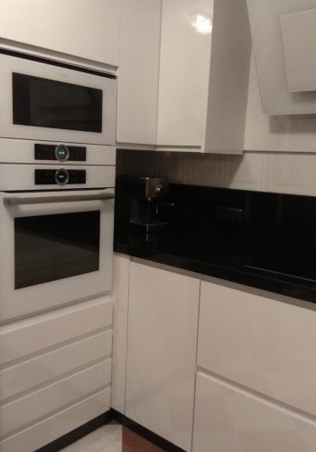 Cocina en blanco brillo, con encimera en granito negro y barra comunicada con el salón 1 (23)